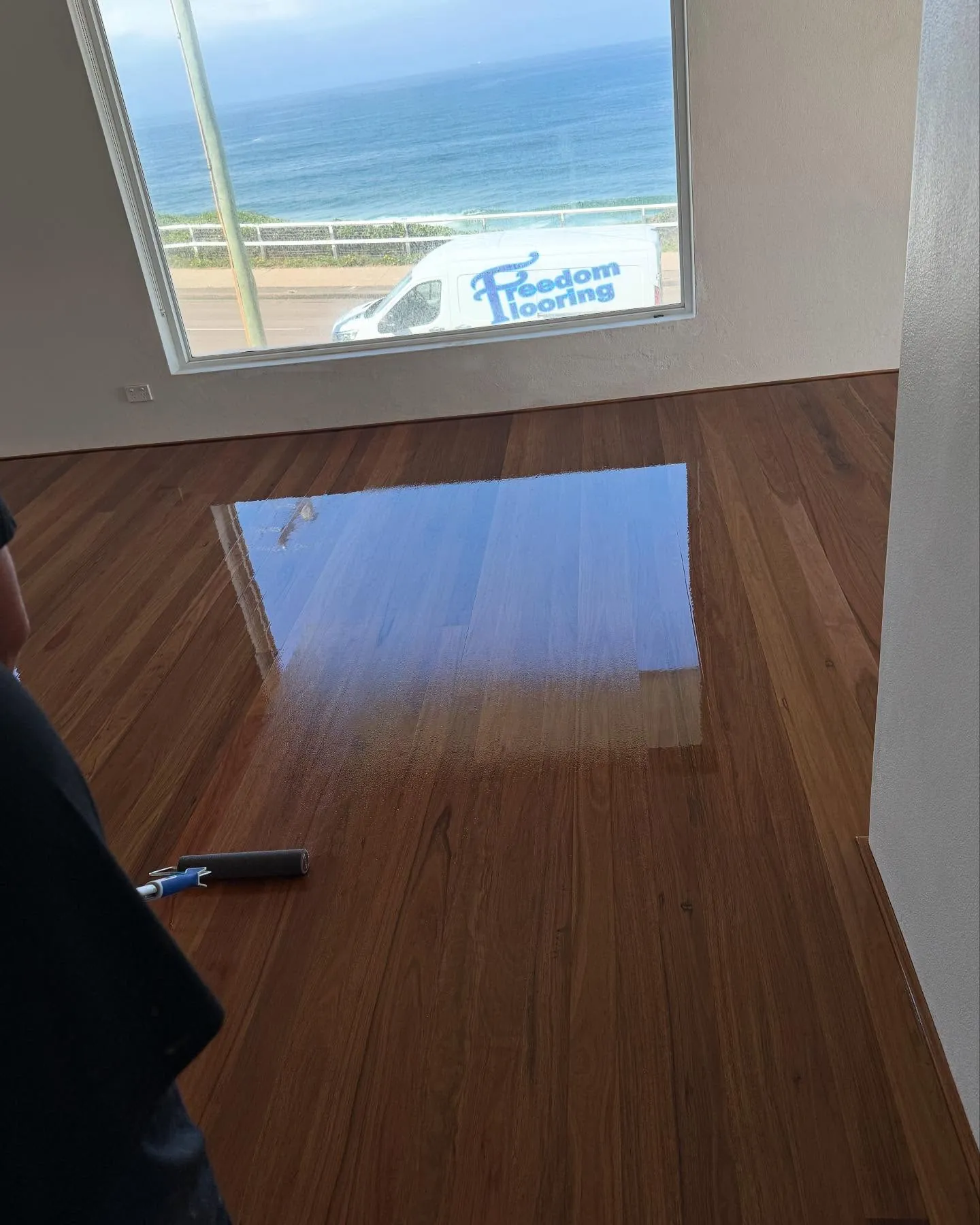 A finished timber floor in an empty room, the Freedom Flooring van parked outside the window