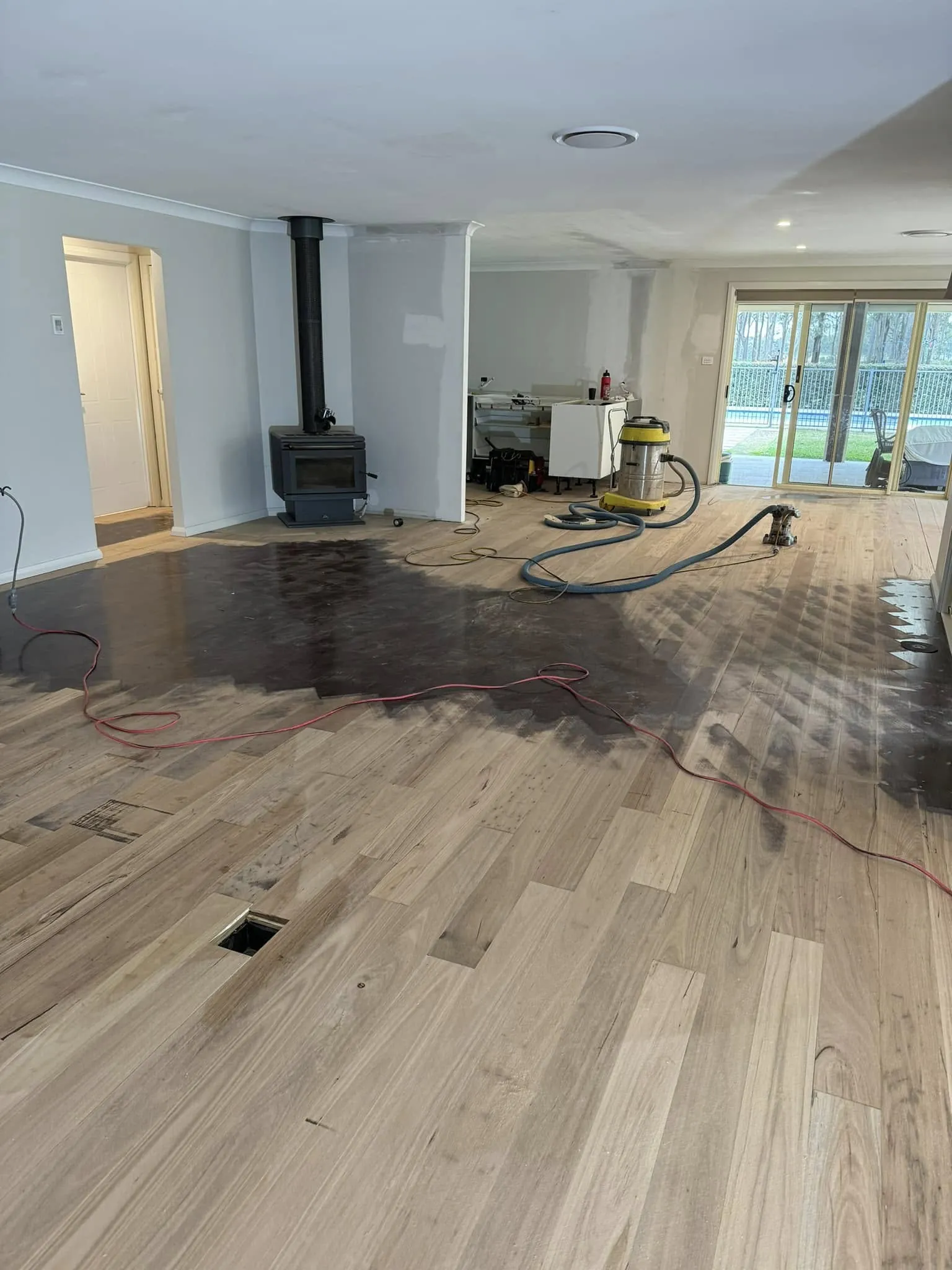 A room mid-restoration where freshly sanded pale boards meet the original dark finish