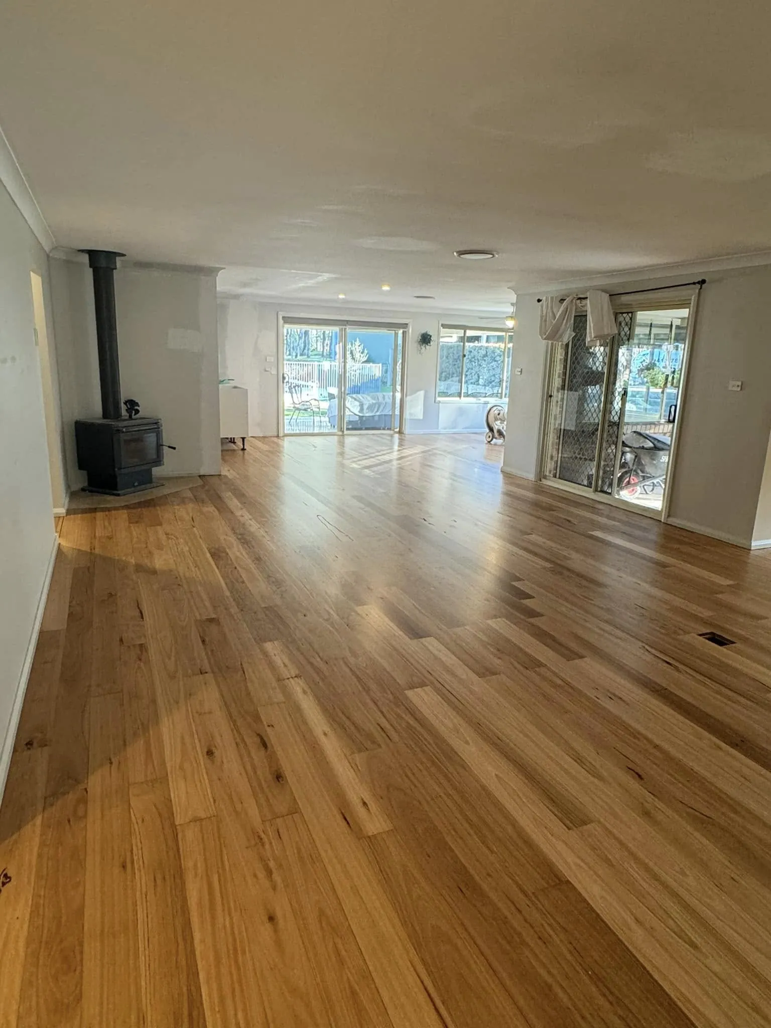 A polished timber floor running through an open-plan room past a wood heater