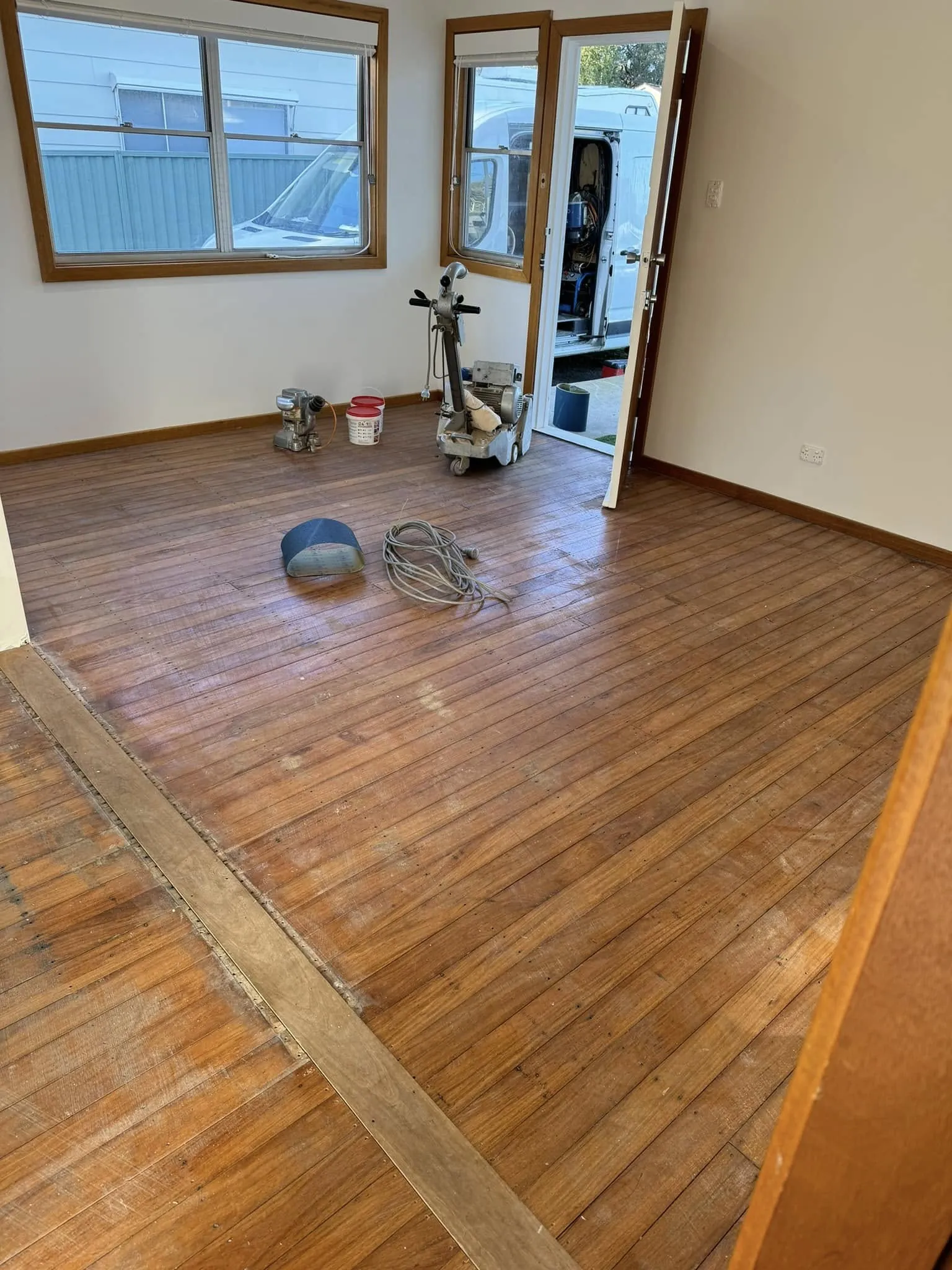 A room part-way through refinishing with tools and coating tins standing on the bare boards