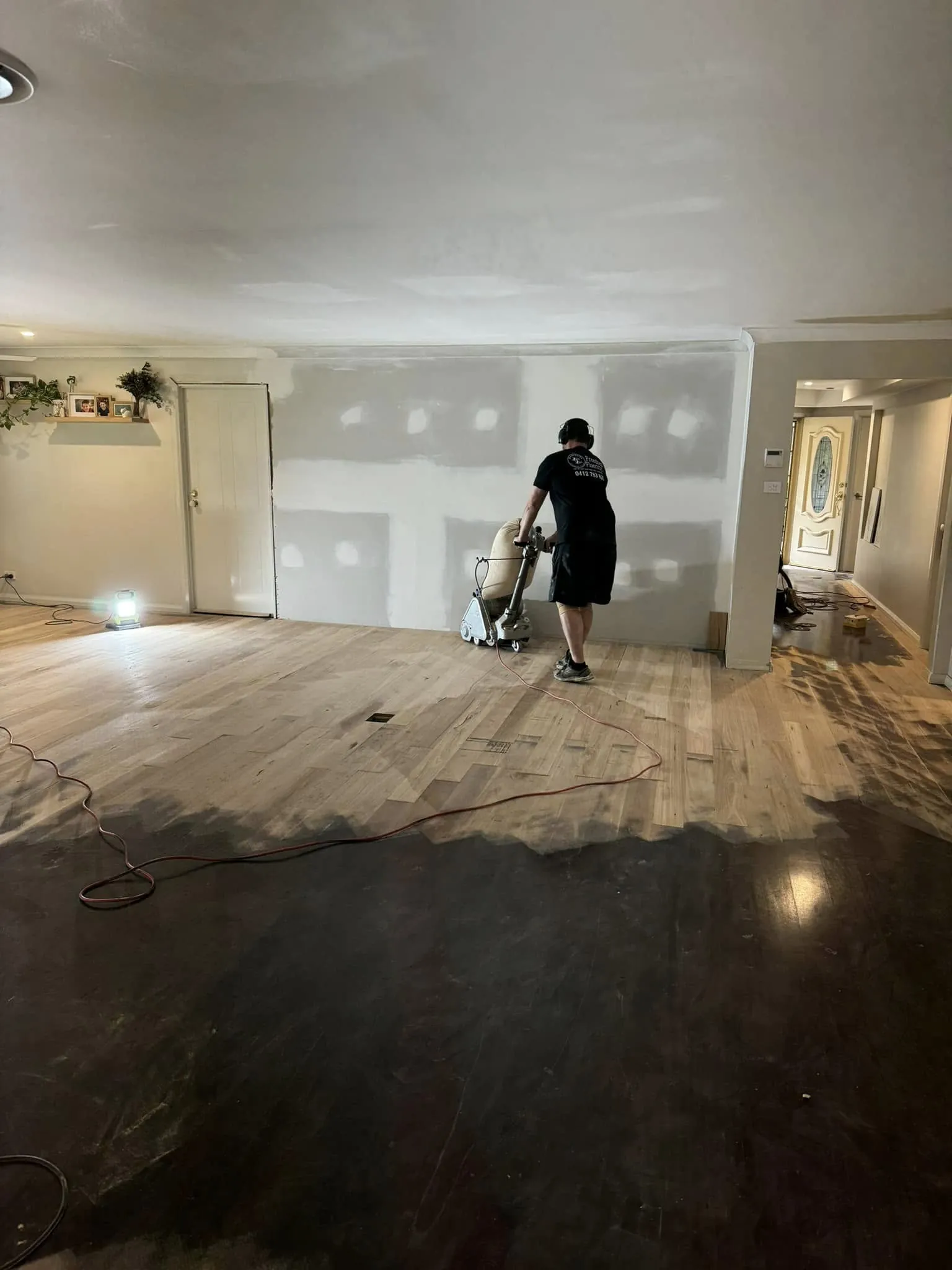 A floor sanding machine working across boards, the sanded section pale against the untouched finish