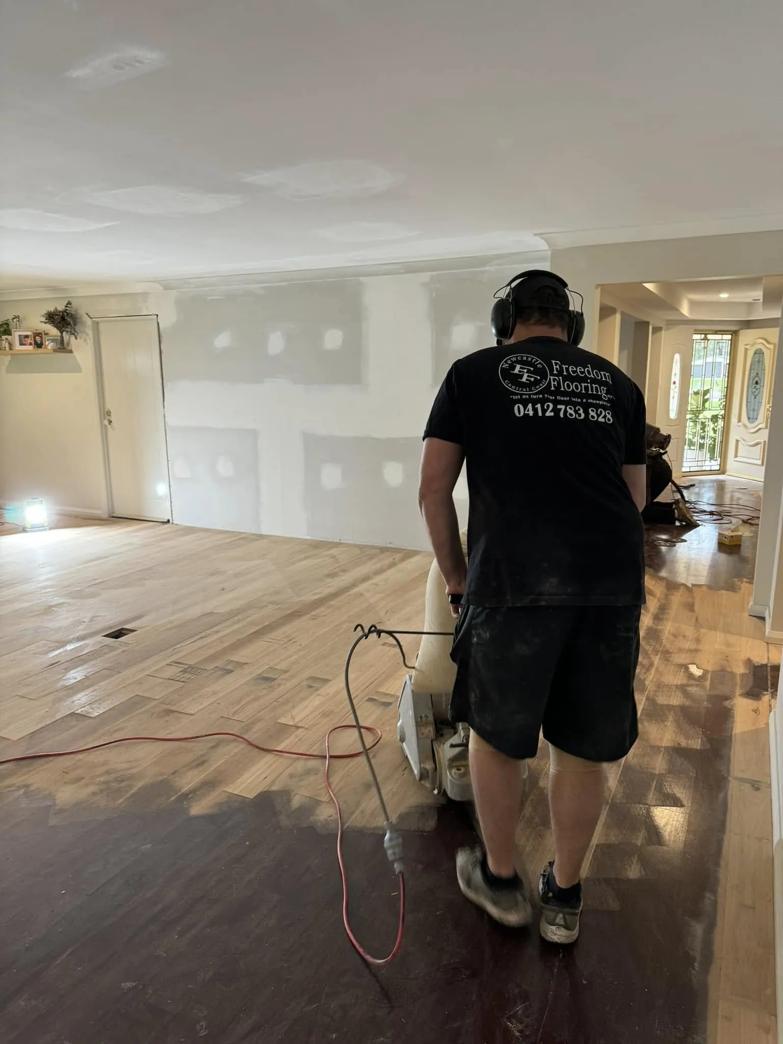 A Freedom Flooring tradesman sanding a timber floor part-way through refinishing