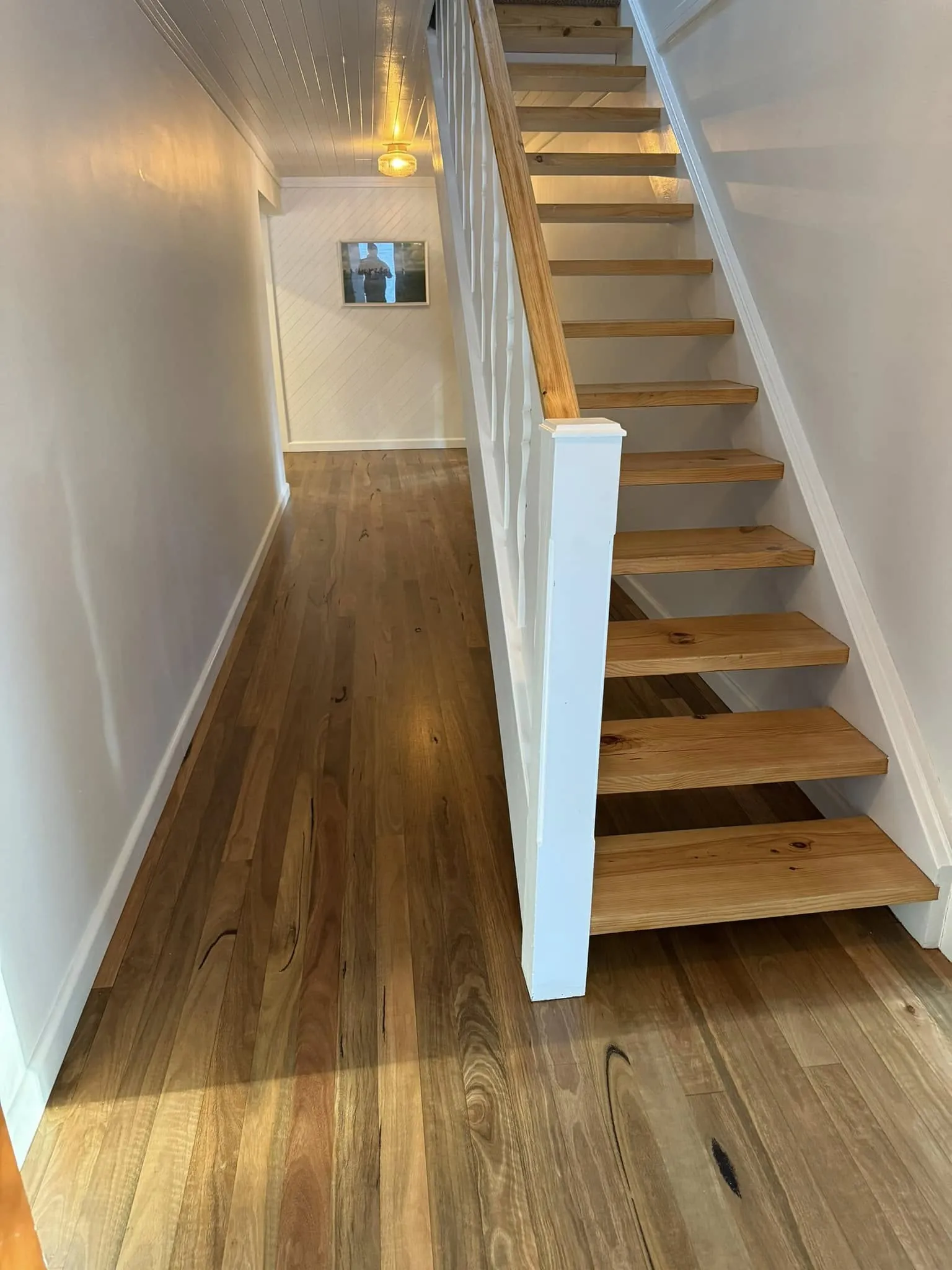 A timber staircase with pale treads and white risers rising from a polished hallway floor