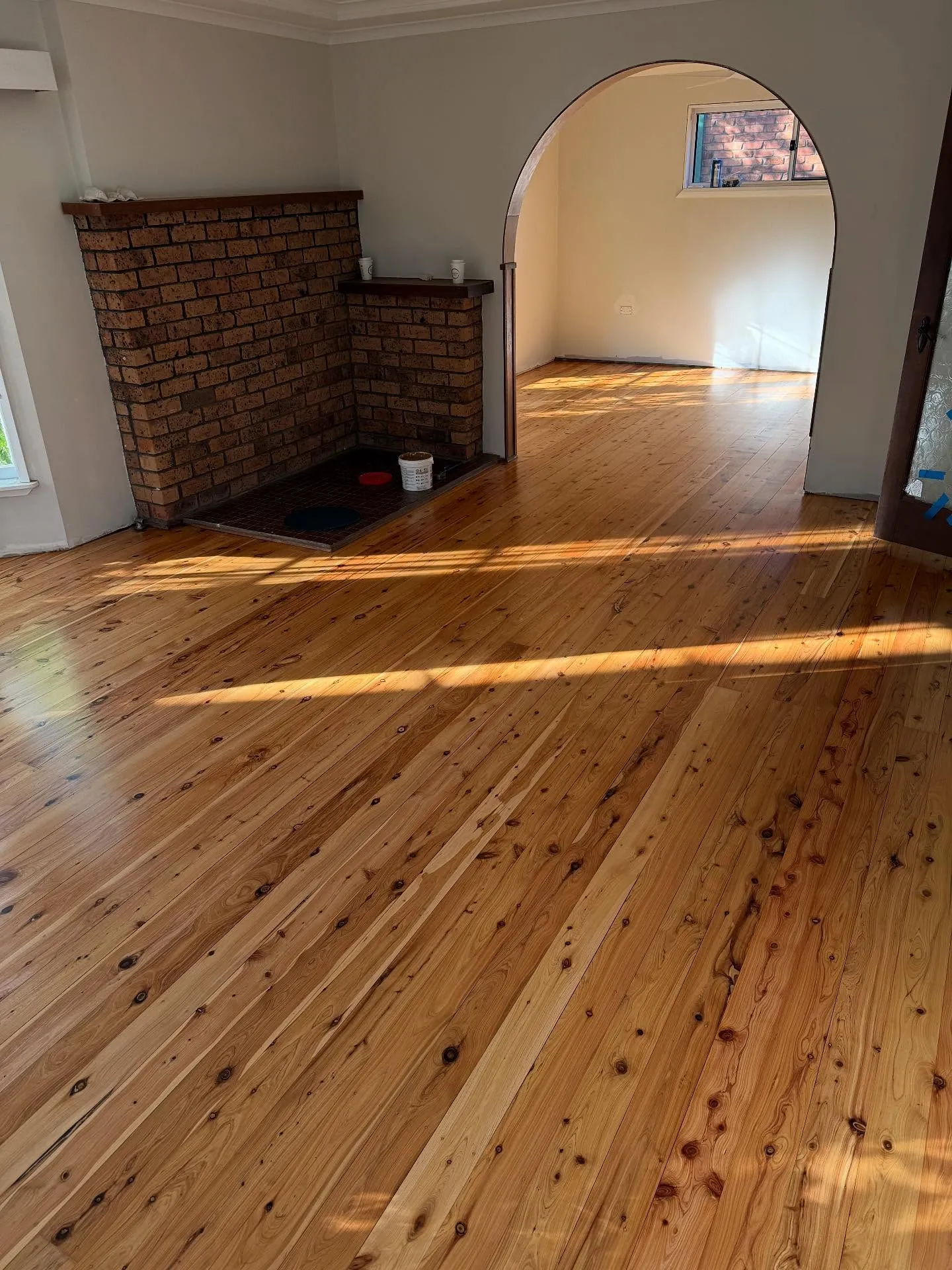 Sunlight falling in bands across a restored pine floor beside a brick fireplace