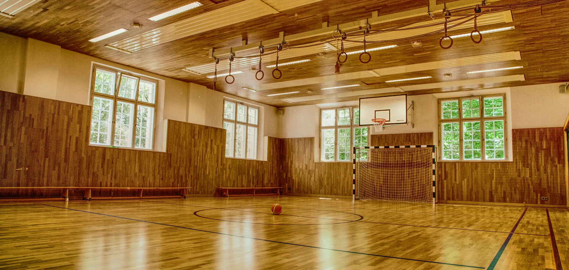 A polished timber sports hall floor marked with court lines beneath high windows