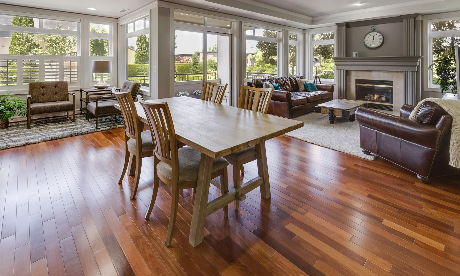 A rich hardwood floor running through an open-plan living and dining room toward tall windows